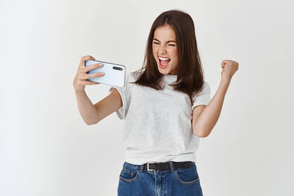 Mlada žena sa radošću gleda svoj mobilni telefon