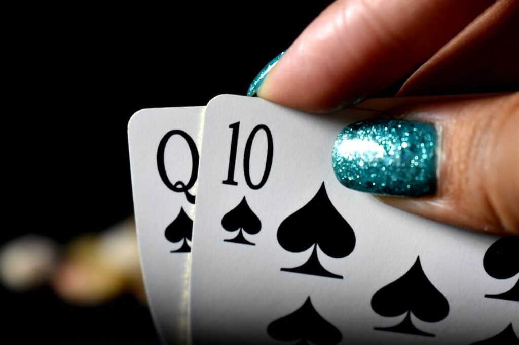 Ženska ruka sa nalakiranim noktima drži karte za poker, Q i 10 u znaki pika