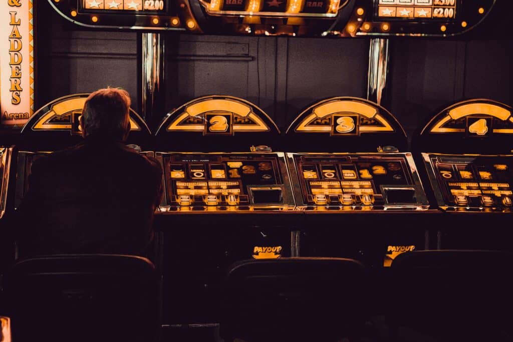 Čovek sedi u zamračenom ambijentu kazina i igra slot aparate