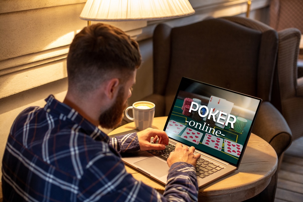 Muškarac u kariranoj košulji sedi ispred laptopa i igra poker online, šolja sa kafom