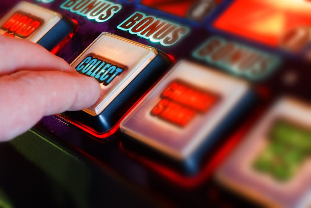 Ruka pritišće dugme na slot aparatu u kazinu, bonus natpis