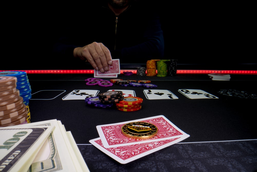 Tamna pozadina, mušakarac drži karte za poker, žetoni na stolu