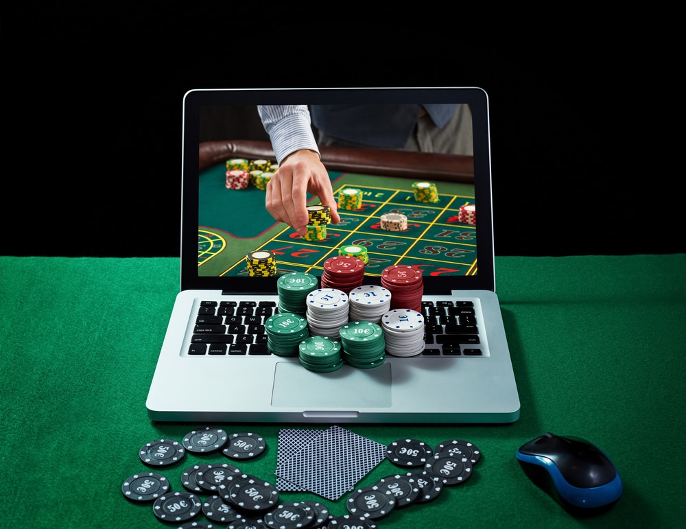 Laptop sa čipovima na brojevima za rulet, zelena podloga, 2 karte okrenute leđima, miš, crna pozadina