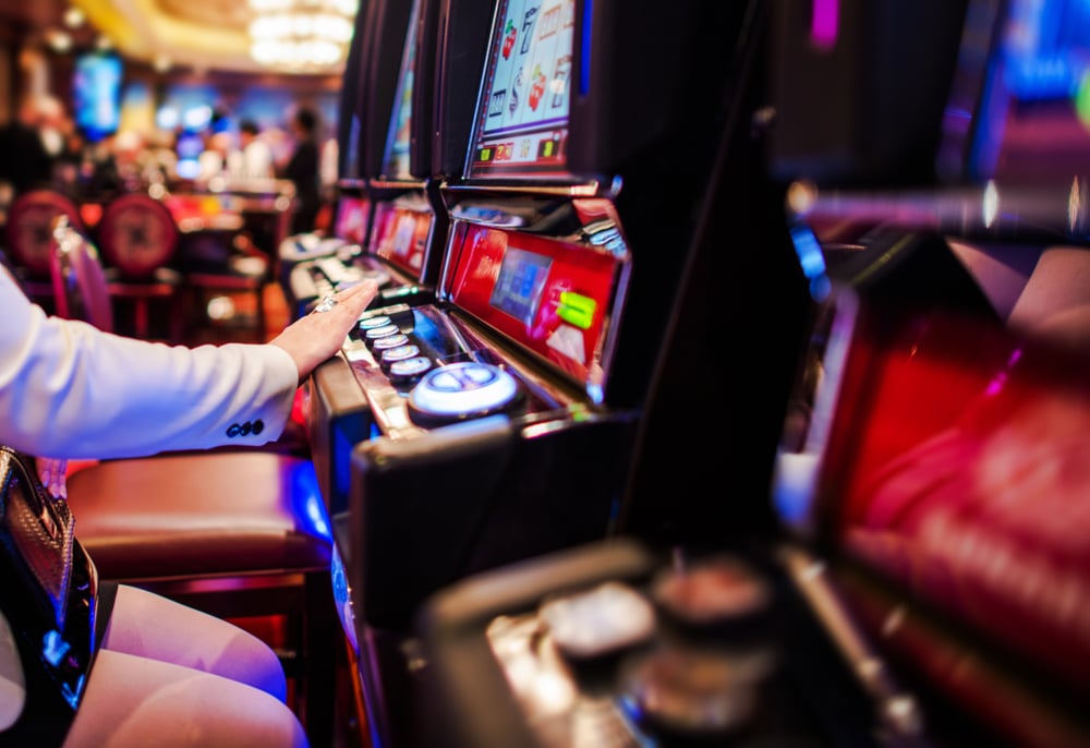 Čovek u kazinu igra slotove na aparatima, mutna pozadina sa još ljudi u kockarnici