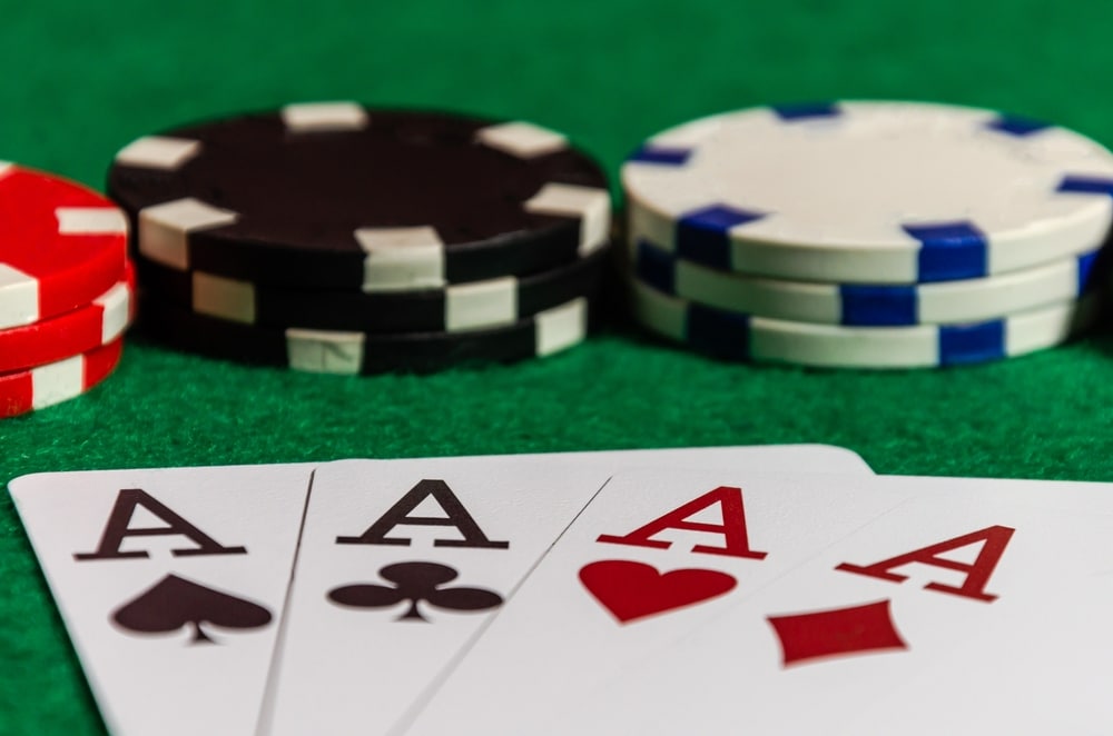 Čipovi za poker na zelenoj pozadini i 4 asa, simboli kartaški, pik, tref, herc, karo.